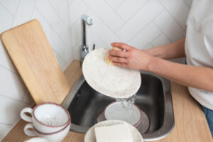 Person washing dishes in sink, showing cleaning zone design with sink and dishwasher for easy cleanup.