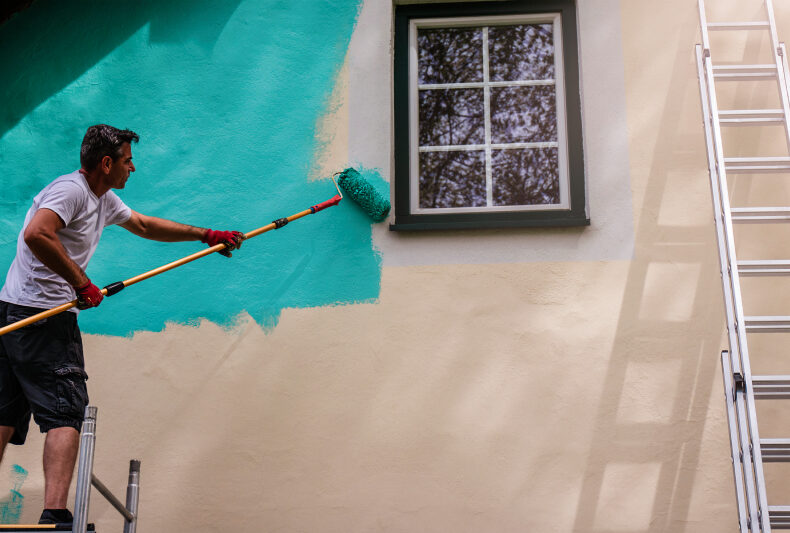 Man painting a house exterior teal, showing how prep work ensures a durable, professional finish.