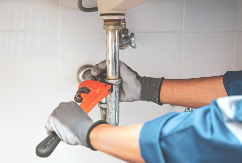 Person using a wrench to repair a pipe, illustrating DIY plumbing repairs and maintenance.