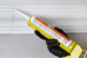 Hand applying caulk to trim, showing how pros seal joints to block moisture and create clean, smooth lines.