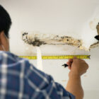 A person measuring ceiling water stains, a sign of roof leaks, with potential mold or paint issues.