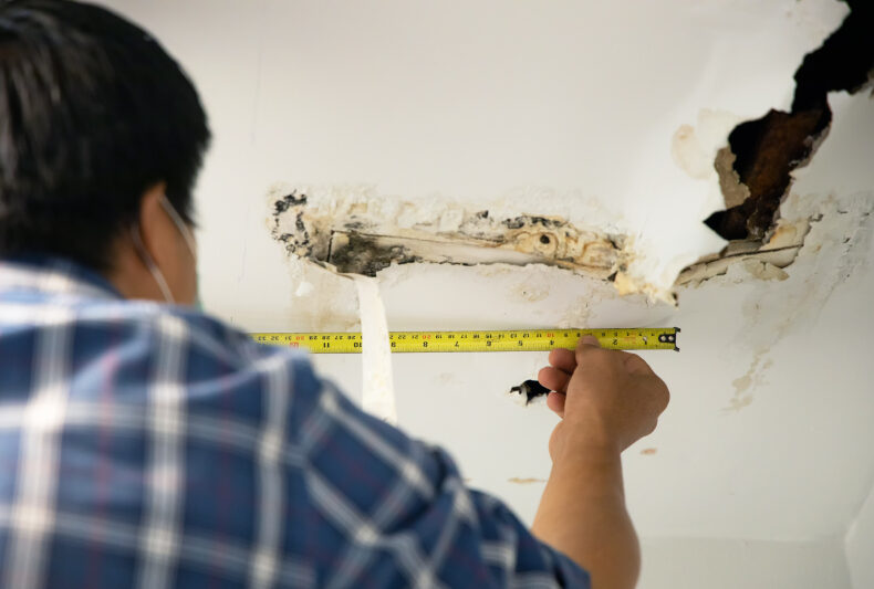 A person measuring ceiling water stains, a sign of roof leaks, with potential mold or paint issues.